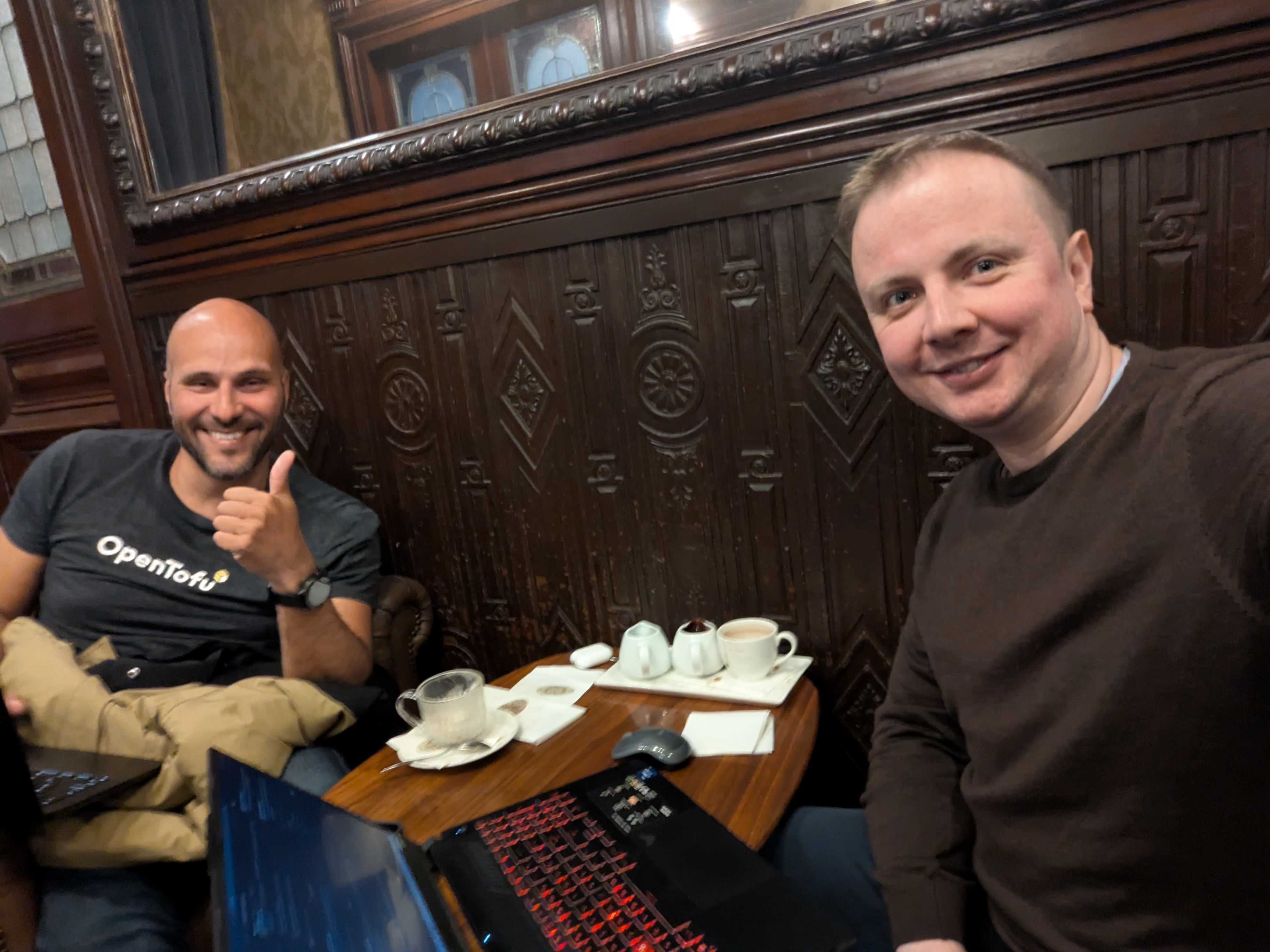 Romaric from Qovery and Jonathan from Tint meeting at Le Train Bleu in Paris, laptops open, discussing the sandboxed AI capabilities Tint built on the Qovery API.